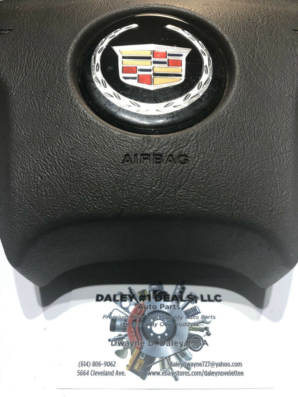 Front view of OEM black driver steering wheel airbag for 2004-2006 Cadillac Escalade with textured cover, Cadillac crest emblem, and embossed AIRBAG text.