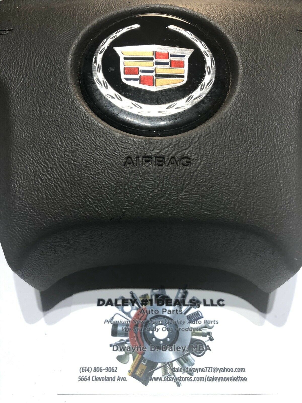 Front view of OEM black driver steering wheel airbag for 2004-2006 Cadillac Escalade with textured cover, Cadillac crest emblem, and embossed AIRBAG text.